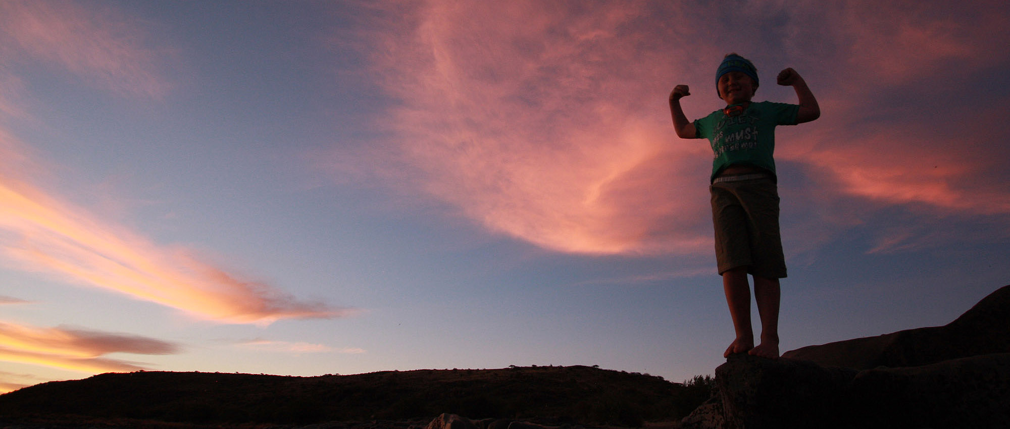 Silhouette of a person standing on a rock at sunset above the river.